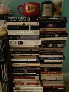 a stack of books sitting on top of a table next to a cup and vase