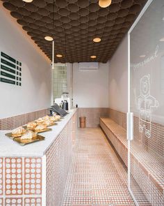 a long counter topped with lots of pastries on top of tiled floor next to a window