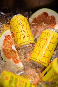 some oranges and grapefruit are sitting on ice with soda cans around them