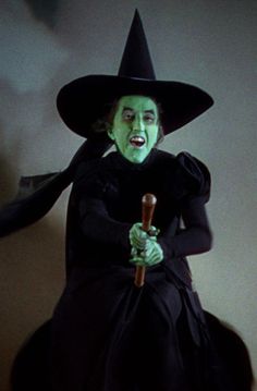 a doll dressed up as a witch holding a broom and wearing a black dress with green paint on it's face