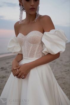 a woman standing on top of a beach next to the ocean wearing a white dress