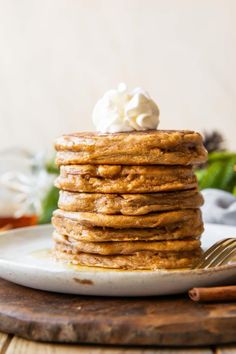 a stack of pancakes with whipped cream on top and cinnamon sticks in the foreground