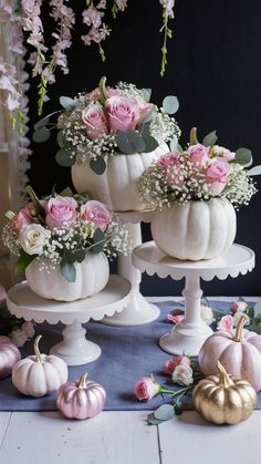 three white pumpkins decorated with flowers and greenery on top of a cake stand