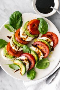 a white plate topped with sliced tomatoes and cucumber slices next to a cup of coffee