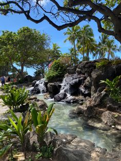 people are walking on the beach next to a waterfall