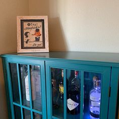 a blue glass cabinet with liquor bottles in it and a framed picture on the wall