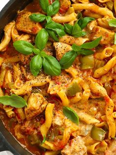 a skillet filled with pasta and meat covered in marinara sauce, basil leaves on top