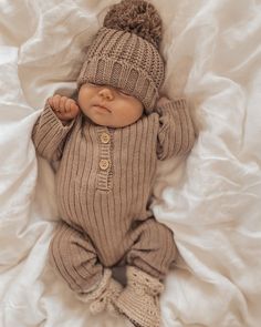 a baby wearing a knitted hat and sweater laying on top of a white sheet