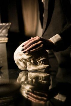 a person with their hand on a fake human skull that is sitting on a table