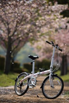 a bicycle parked on the side of a dirt road next to trees with pink flowers