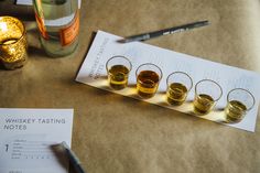 there are five glasses on the table next to a bottle and some papers with writing