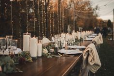 a long table with candles, plates and napkins is set for an outdoor dinner