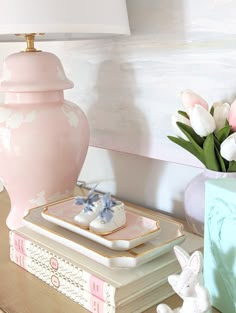 a pink vase sitting on top of a wooden table next to a lamp and plate