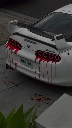 a white toyota sports car with blood on the hood and tail lights is parked in front of a building