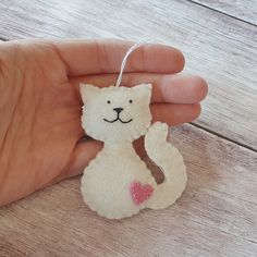 a hand holding a small white cat ornament with a pink heart on it