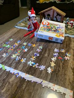 an elf sitting on top of a wooden table next to a puzzle box filled with colorful pieces