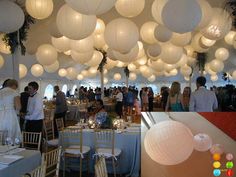 many people are gathered around tables with white paper lanterns hanging from the ceiling