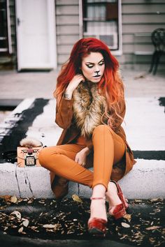 a woman with red hair and makeup is sitting on the curb