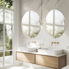 two round mirrors are above the double sinks in this bathroom with marble walls and flooring