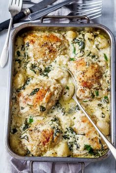 a casserole dish with chicken, spinach and cheese in it next to silverware