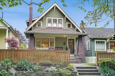 a house with green siding and brown trim on the front porch is surrounded by greenery