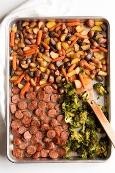 a pan filled with sausage and broccoli next to a wooden spoon on a white surface