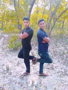 two men are standing in the sand with their arms crossed