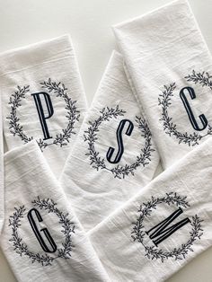 three white towels with black monogrammed letters and wreaths on them, sitting next to each other