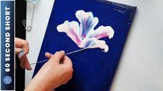 a person is painting a flower on a blue piece of paper with white and pink paint