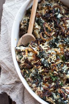 a white bowl filled with spinach, cheese and other toppings next to a wooden spoon