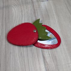 a red mirror sitting on top of a wooden table next to a green apple shaped object