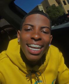 a young man wearing a yellow hoodie smiles at the camera while sitting in his car