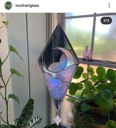 a stained glass sun catcher hanging on a window sill next to potted plants