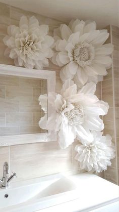 a white sink sitting under a mirror next to a wall with flowers on the wall