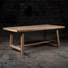 a wooden table sitting on top of a stone floor next to a black brick wall