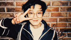 a young man wearing glasses making the vulcan sign with his hand while standing in front of a brick wall