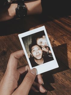 a person holding up a polaroid with an image of two people on it's side