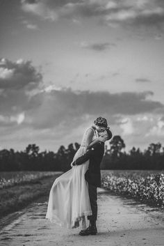 a bride and groom kissing in the middle of a dirt road with cotton fields behind them