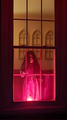 a person in a ghost costume standing behind a window with pink light shining through it