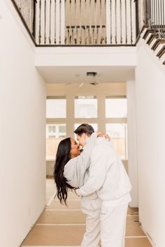 a man and woman are kissing in an empty room with stairs leading up to the second floor