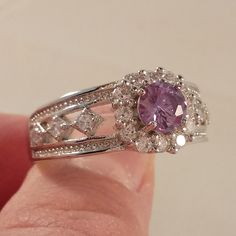 a close up of a person's hand holding a ring with a purple stone