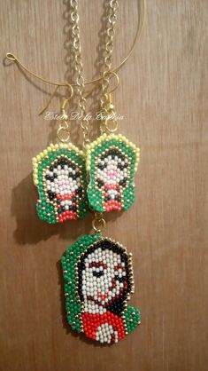 two pieces of bead art hanging from chains on a wooden surface, one has a face and the other has an earring