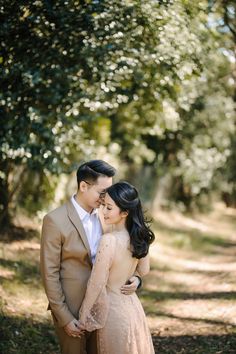 a man and woman standing next to each other on a dirt road in front of trees