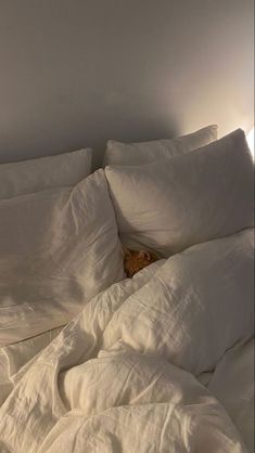 an unmade bed with white linens and a cat laying on the bottom half