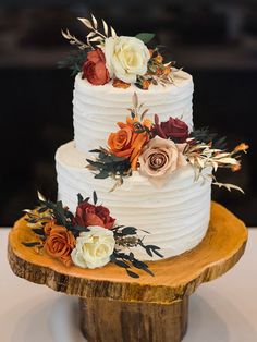 a three tiered white cake with flowers on it sitting on top of a wooden stand