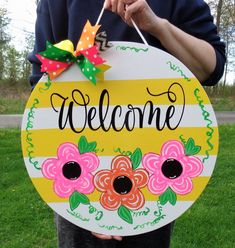 a person holding up a welcome sign with flowers painted on the front and side of it