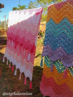 two crocheted afghans hanging on clothes line in the grass with trees in the background