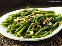 a white plate topped with green beans covered in nuts and seasoning on top of a table