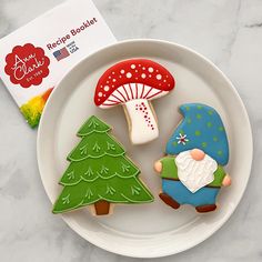 three decorated cookies sitting on top of a white plate next to a book and a mushroom