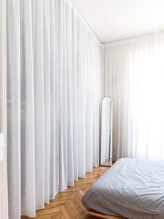 a bedroom with white drapes on the wall and wooden flooring, along with a bed